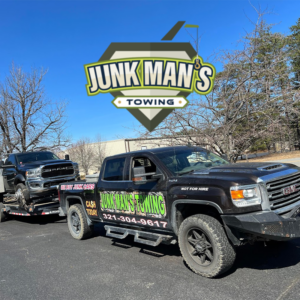 Junk Man's Towing pickup hauling a damaged truck on a flatbed, company logo above