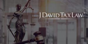 Lady Justice statue and gavel before a modern office backdrop, with the J David Tax Law logo glowing at right