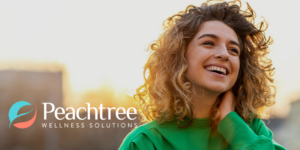 Smiling woman with curly hair in a green sweater at sunset outdoors, with Peachtree Wellness Solutions logo