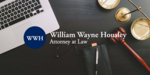 Laptop, scales of justice, gavel, and notebook on dark desk, with William Wayne Housley law logo overlay