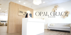 Bright salon reception with white front desk, slatted wood wall, pampas decor, sofa, and Opal Grace signage