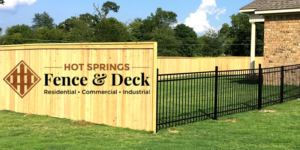 Backyard with wooden privacy fence and black metal fence by brick house, Hot Springs Fence & Deck logo overlay