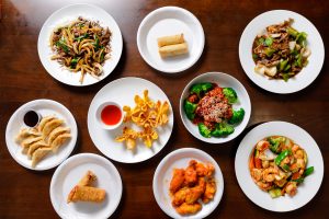 Overhead view of assorted Asian dishes: dumplings, noodles, broccoli chicken, shrimp stir-fry, wings, sauces