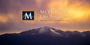 Snow-capped mountain range under dramatic sunset sky with McDowell Law Firm LLC logo centered above the peaks
