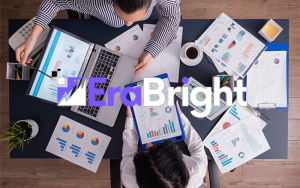 Overhead view of two colleagues analyzing reports with laptops, charts, and coffee, EraBright logo overlay
