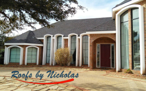 Elegant house with tall arched windows and red door, wide driveway, logo reading Roofs by Nicholas in script